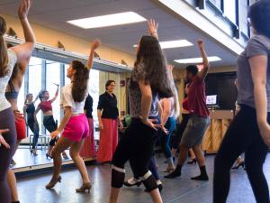 A group of high school students are in a dance studio practicing a dance routine for a musical.