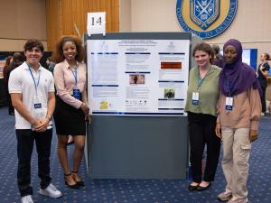 Four students are standing in front of their research poster smiling.