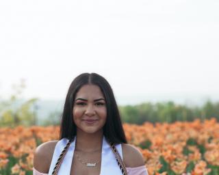 individual smiling in front of a garden of flowers wearing graduation stoles and cords