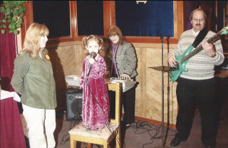 young girl stands on a chair with a microphone to her mouth. 