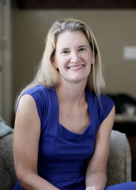 A caucasian, blonde woman sits and smiles at the camera. 