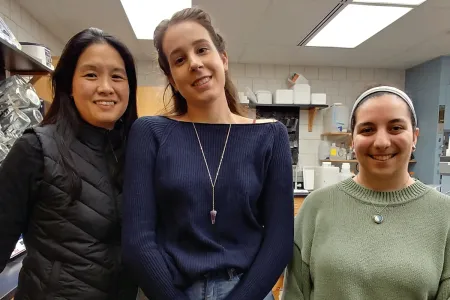 Three women stand shoulder-to-shoulder in a laboratory. 