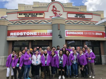 A group of people in pink jackets pose in front of a building