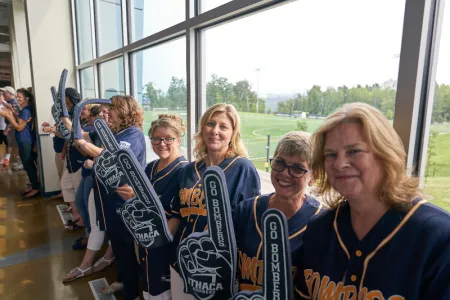 A group of smiling IC staff members stand in a brightly lit hallway to welcome new students at Convocation 2018.