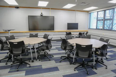 Classroom with tables and chairs on casters, computer monitors and large interactive display
