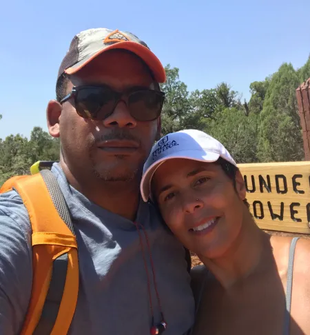 President Shirley M. Collado and her husband A. Van Jordan wear outdoor hiking gear and stand near a sign for a trailhead.