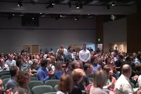 People standing while a crowd of seated people applaud