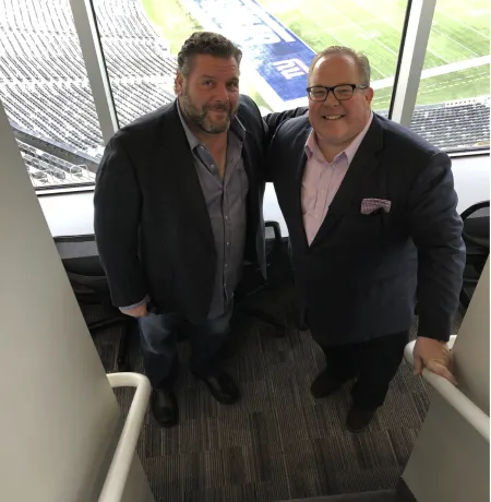 Two men pose for a photo in a football stadium
