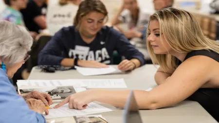 two students working at table with older adult