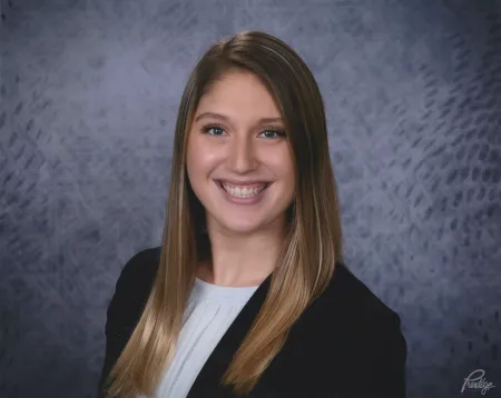 This is a photo of Angelina Domena. Angelina is wearing a blue blazer with a white shirt underneath. Angelina has long brown hair over the shoulders.