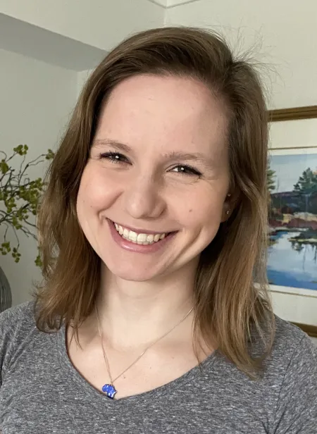 This is a photo of Ashley Warren. Ashley is wearing a gray shirt with a blue locket necklace.