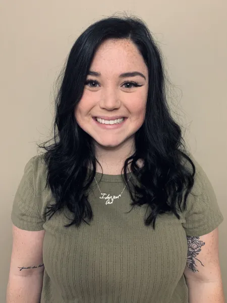 This is a photo of Casey Wrobel. Casey is wearing a short green shirt with a silver necklace. Casey's hair is long and black.