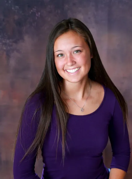 This is a photo of Elizabeth Gee. Elizabeth is wearing a long sleeve purple shirt with a silver necklace. Elizabeth's hair is long and dark.