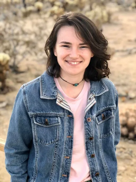This is a photo of Julia Frisch. Julia is wearing a blue jean jacket over a pink shirt with a choker necklace.