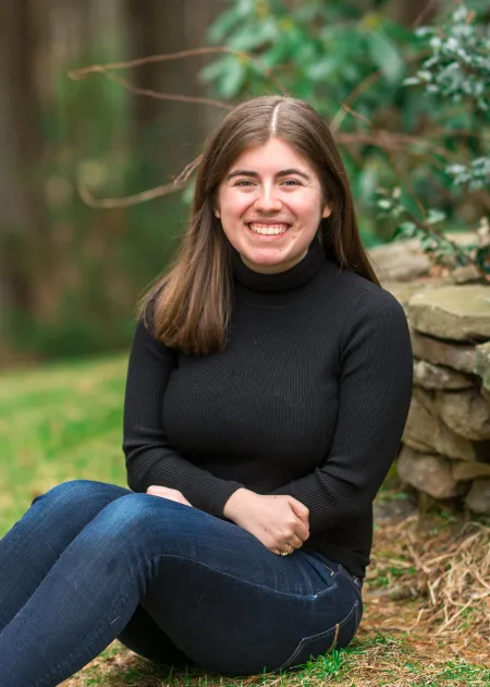This is a photo of Lucy Hemingway seated on the grass wearing a long sleeve black turtleneck and jeans.