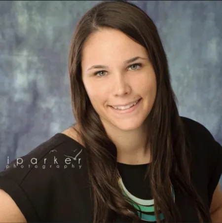 This is a photo of Tara Schoor. Tara is wearing a short sleeve black shirt and has long dark hair. The photo background is a gray color.