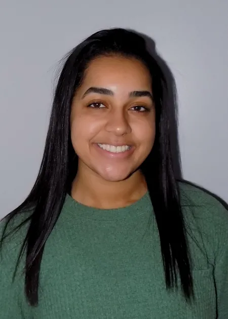 This is a photo of Taylor Larkin. Taylor is smiling at the camera with long black hair over the shoulders. Taylor is wearing a long sleeve green shirt.