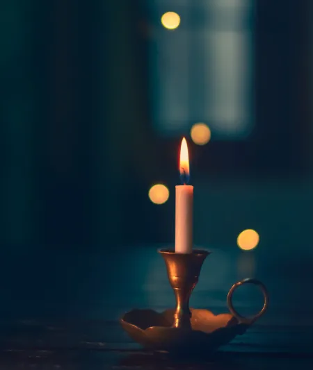 White candle lit on brass candle holder against nighttime 