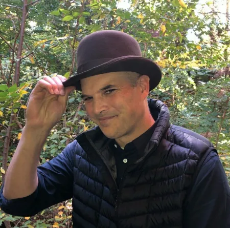 man wearing a vest and a bowler hat outside