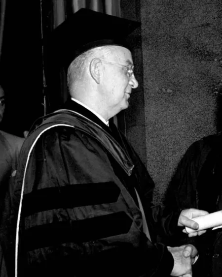 Black and white photo; in academic cap and gown.