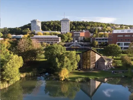 Photo of pond, trees, and six campus buildings. 