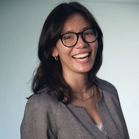 Julia is looking at the camera and smiling widely. She is wearing a heather grey suit jacket and black rimmed glasses.