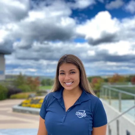 Samantha is smiling directly at the camera wearing a blue Ithaca College polo shirt.