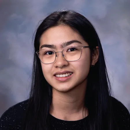 Phung is sitting, looking at the camera, and smiling. She is wearing glasses and a black top. Her long, dark hair is parted down the middle.
