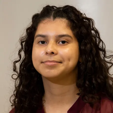 Alma is looking at the camera wearing a dark red blouse.