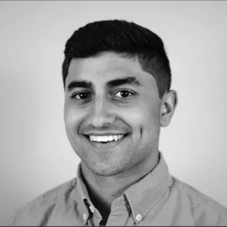 Jordan is smiling at the camera wearing a button up shirt and short cropped hair. The picture is in grey scale.