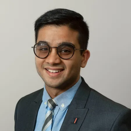 Abhinav is smiling at the camera wearing a blue suit and tie and black rimmed glasses.
