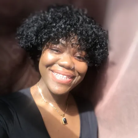 Serah is smiling at the camera wearing a black top. Her hair is curly with bangs.