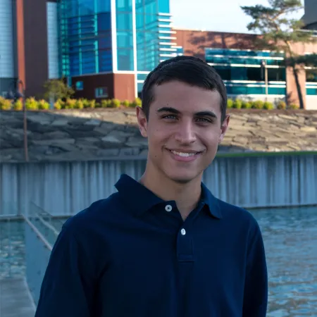 Manny is standing in front of the IC Fountains smiling at the camera. He is wearing a navy blue polo shirt.