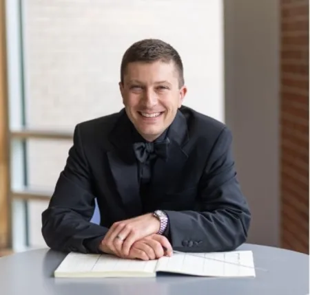 Man in a suit smiling holding a baton