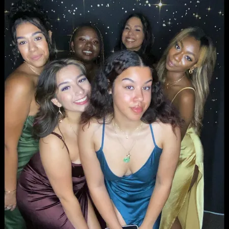 Nathalie is posed in a group photo with five other individuals. Nathalie is positioned second from the left and is wearing a burgundy dress. Nathalie is looking at the camera and is smiling.