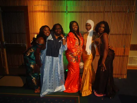 Sarake is posing for a group photo. She is second from the right in the picture, wearing a yellow dress and white hijab.