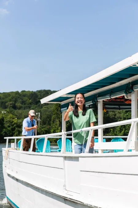 A woman on the deck of a boat gives a thumbs up sign.
