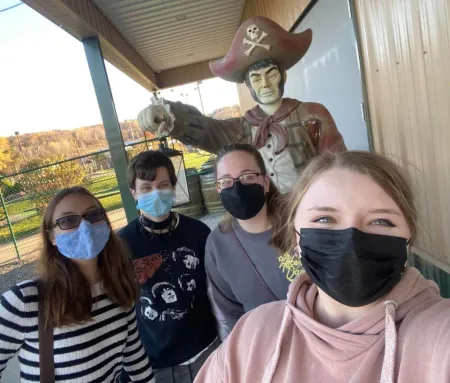 a group of students wearing masks poses in front of a statue of a pirate
