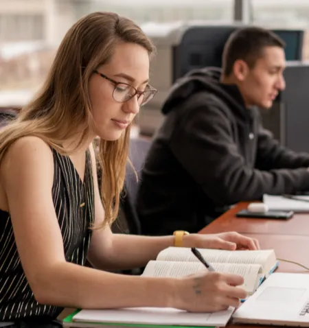 A female student takes notes as she reads a book