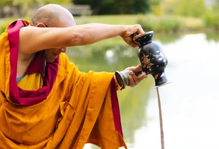 a monk pours the sand used in the mandala into the pond
