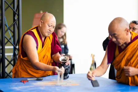 two monks pick up the sand used to create the mandala