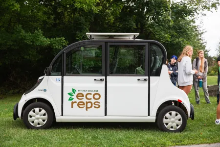 A small, white solar-powered car with "Ithaca College Eco Reps" branded on the side. 