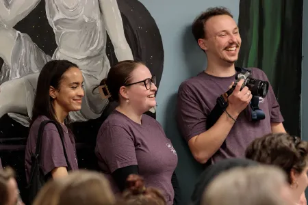College students wearing matching purple shirts laugh at an event. 