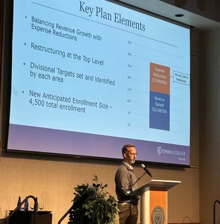 Man stands at lectern with slide projected behind him.