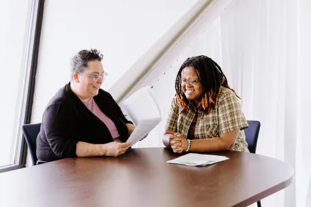 A professor and college student laugh together at a table. 