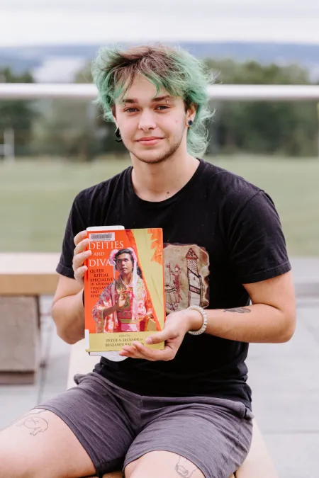 A college student holds up a book. 