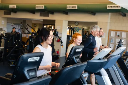 An intergenerational group of people run on treadmills. 