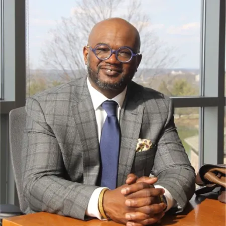 Headshot of Christopher House. He is wearing a grey checkerboard suite with a white dress shirt and blue tie and glasses.