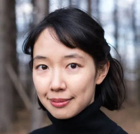 Headshot of Christine Kitano. Christine is wearing a black turtleneck sweater. Christine is posed in front of trees in winter.