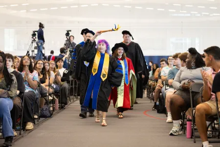 People wearing academic regalia walk among a large group of students. 